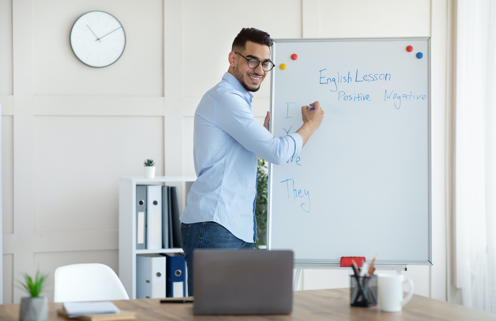 Arab male teacher giving online English lesson, writing grammar rules on blackboard. Distance